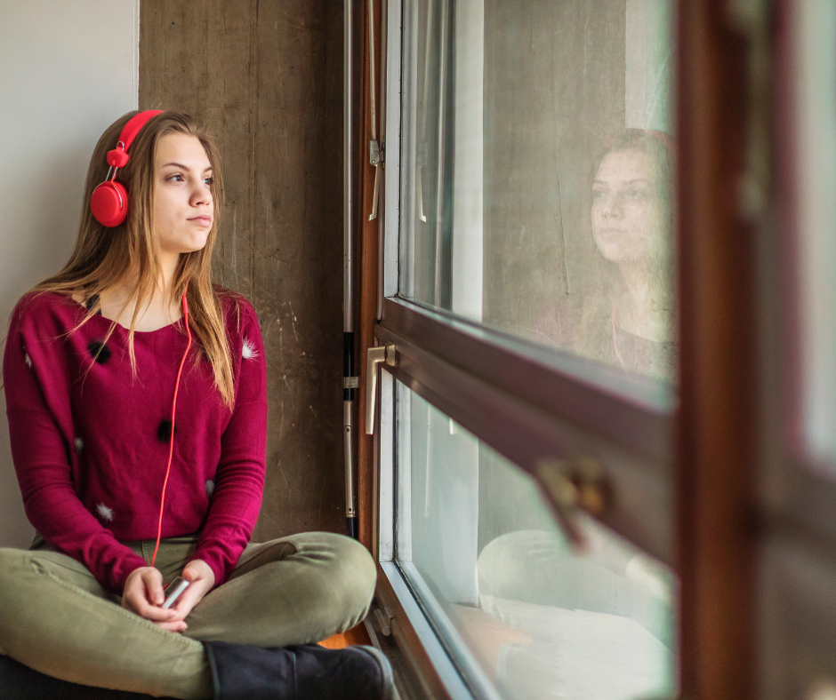 młoda dziewczyna ze słuchawkami na uszach siedząca przy oknie